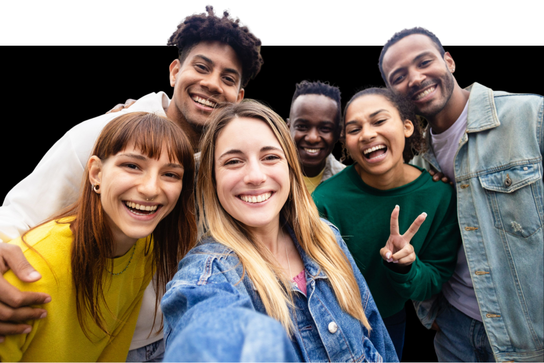 A group of six smiling people take a selfie together. One person is holding up a peace sign.