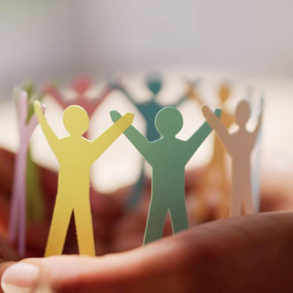 Hands holding a circle of colorful paper cut-out figures with arms raised, symbolizing unity and community.